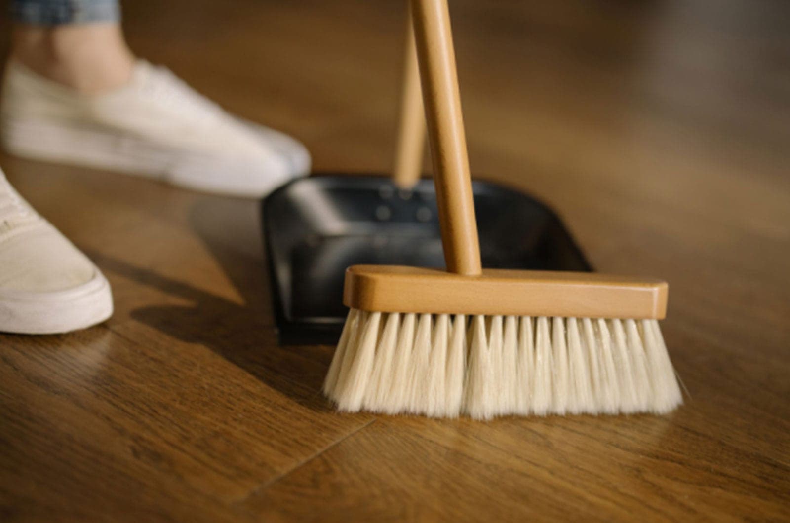 A woman with a broom sweeping into a dustpan