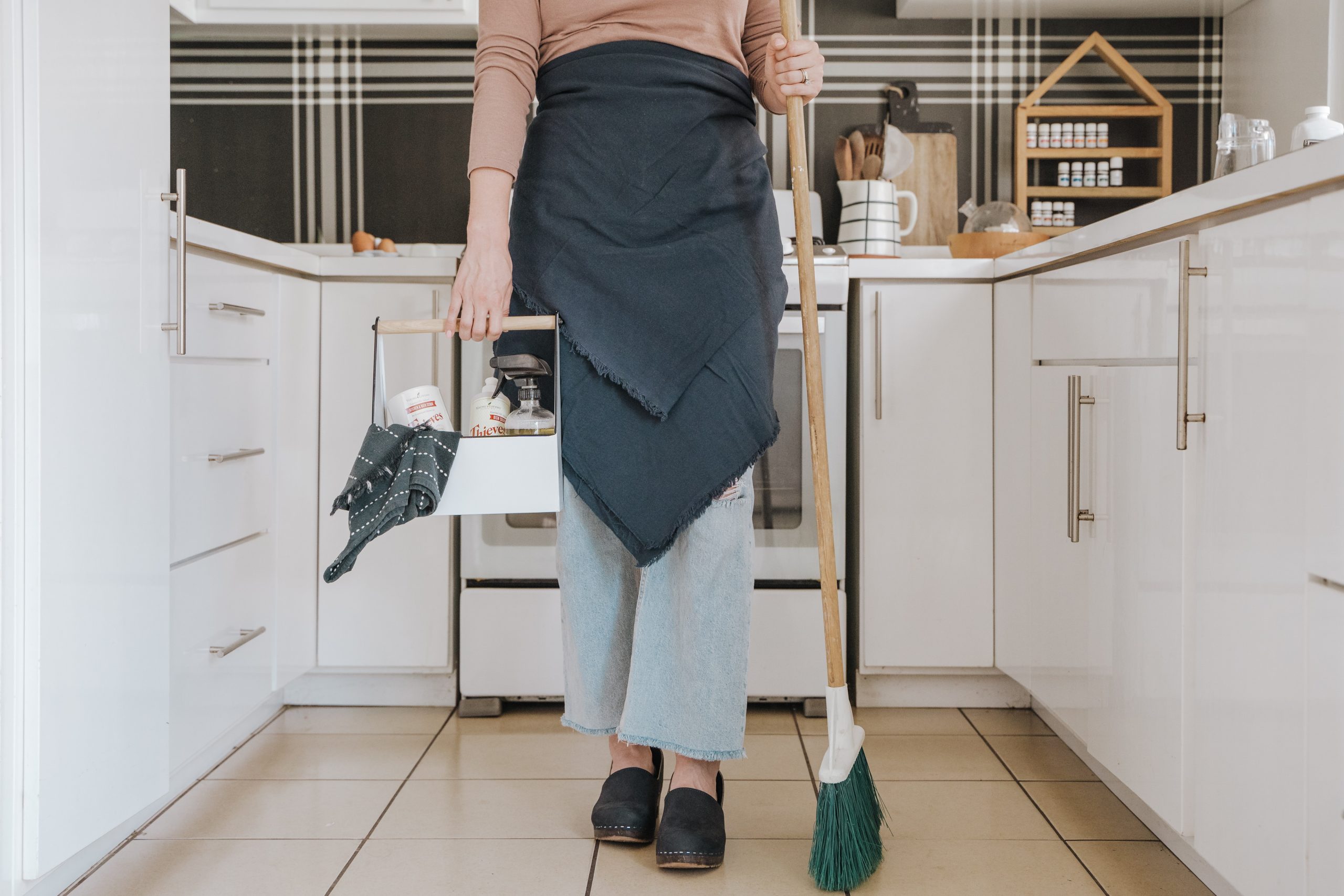 Woman standing in a kitchen holding cleaning supplies
